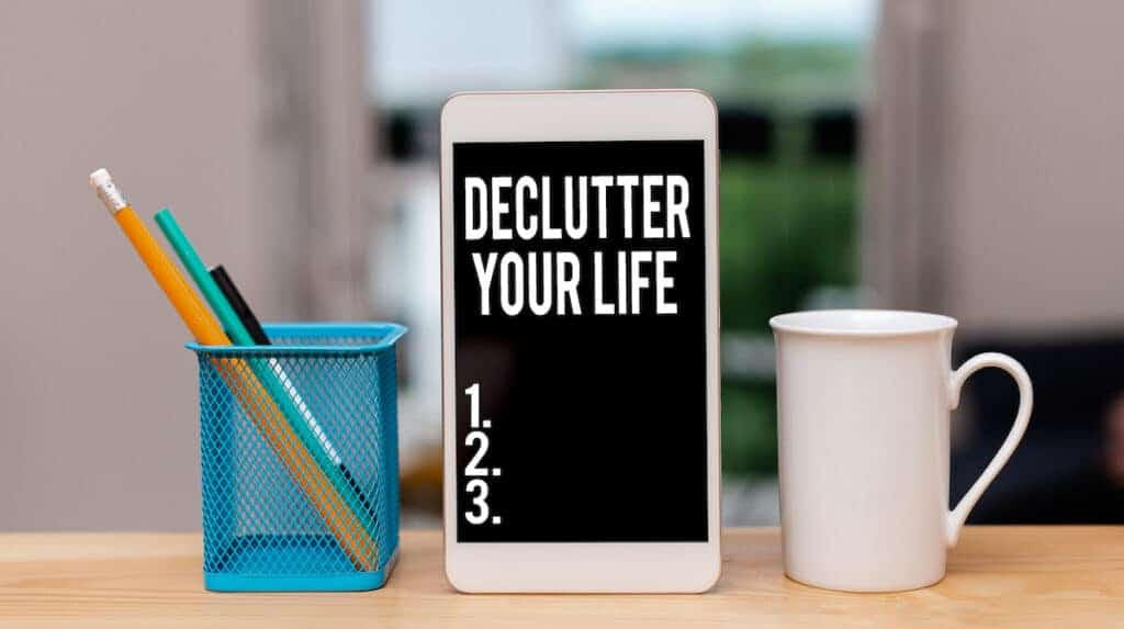 A photo of a desk holding a pencil cup, white mug and phone with "Declutter Your Life" on the screen. This represents digitally decluttering.