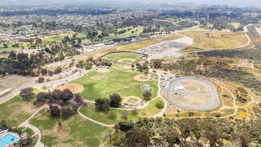 High-angle aerial view of Morley Field in North Park, showing the baseball diamonds, San Diego Velodrome, and the expansive canyon landscape leading toward the city.