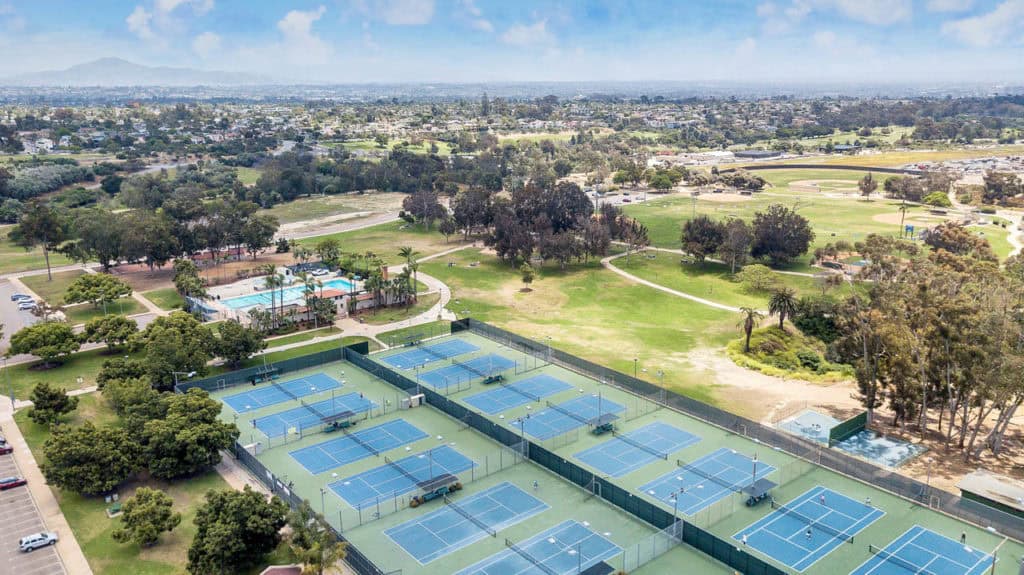Aerial view of the Balboa Tennis Club and Morley Field Sports Complex in North Park, showing the expansive blue tennis courts, swimming pool, and baseball diamonds set against the San Diego landscape.