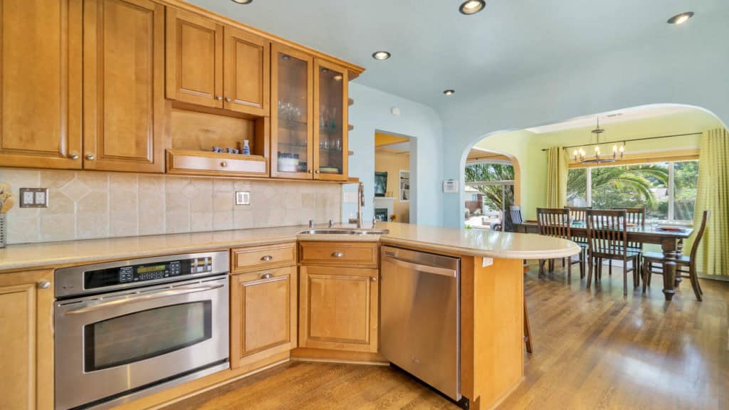 Modern kitchen at 2212 Myrtle Ave in North Park with wood cabinets, stainless steel appliances, and a light blue ceiling, looking through an archway into the lime green dining room.