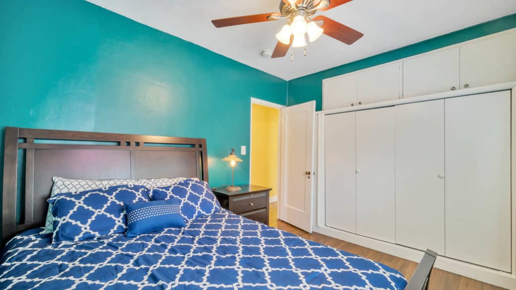Bedroom at 2212 Myrtle Ave in North Park featuring teal walls, a dark wood headboard, and a large white built-in closet with additional overhead storage cabinets.