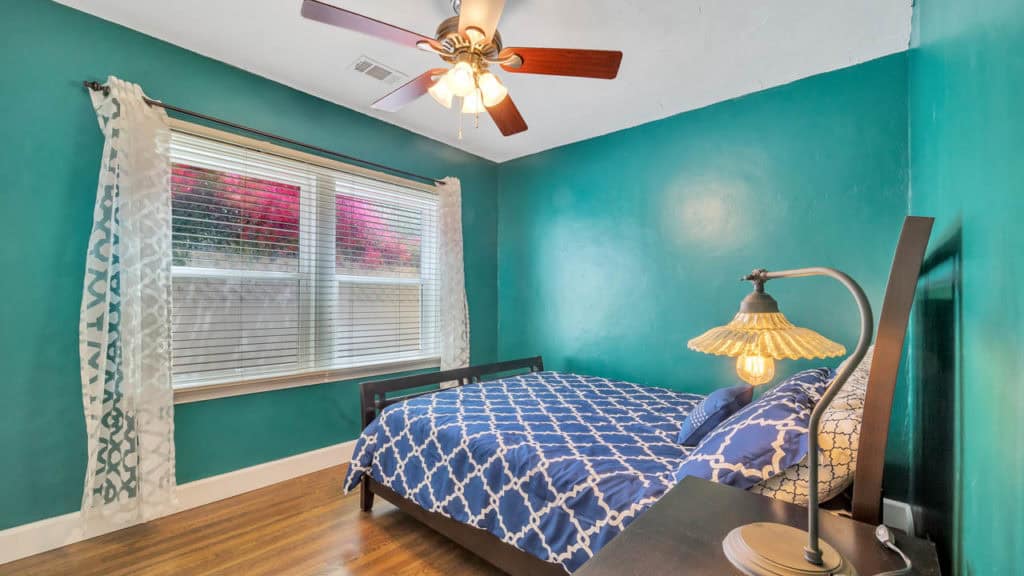 Bedroom at 2212 Myrtle Ave in North Park featuring teal walls, hardwood floors, a dark wood bed with a blue geometric comforter, and a window with white curtains.
