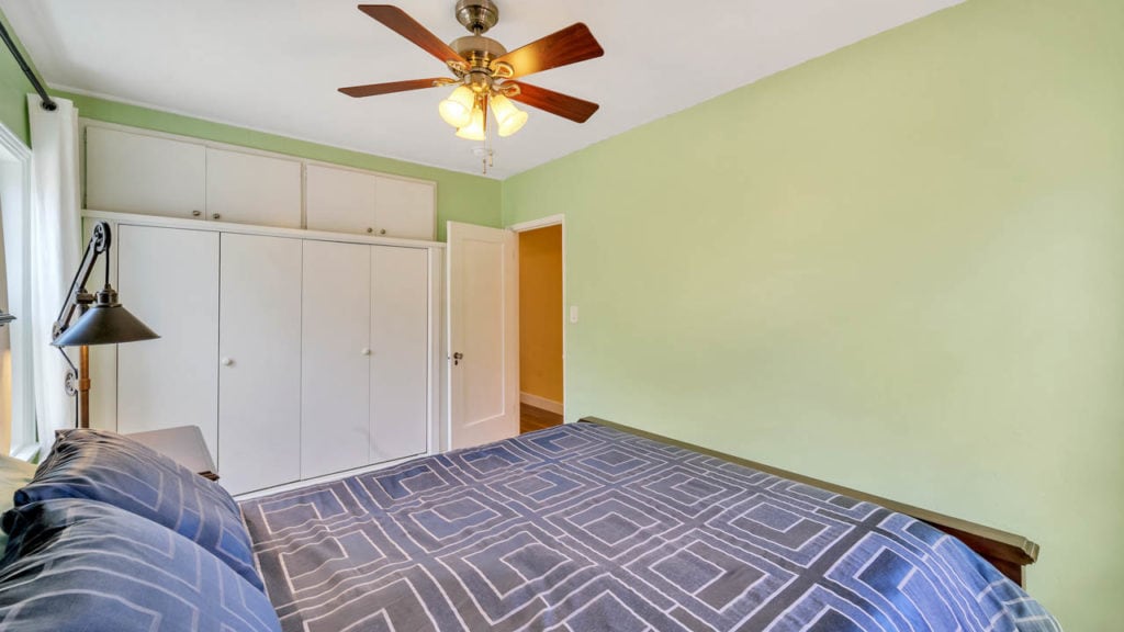 Bedroom at 2212 Myrtle Ave in North Park featuring sage green walls, a white built-in closet with overhead storage, and a bed with a blue geometric patterned comforter.