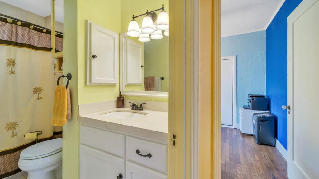 Interior view at 2212 Myrtle Ave in North Park showing a lime green bathroom with a white vanity next to a hallway leading to a bright blue accent wall and office area.