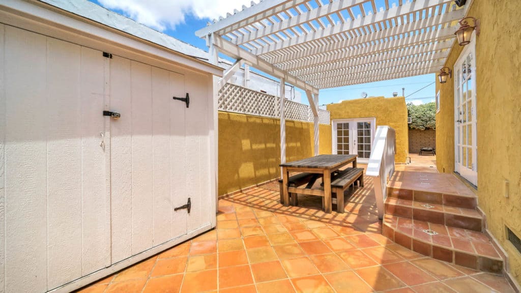 Yellow Spanish Revival home at 2212 Myrtle Ave in North Park showing a private terracotta patio with a white storage shed, pergola, and outdoor dining table.