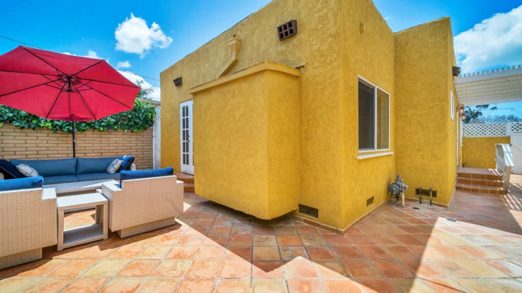 Yellow Spanish Revival home at 2212 Myrtle Ave in North Park featuring a terracotta tile patio with a blue outdoor sectional and a red umbrella.