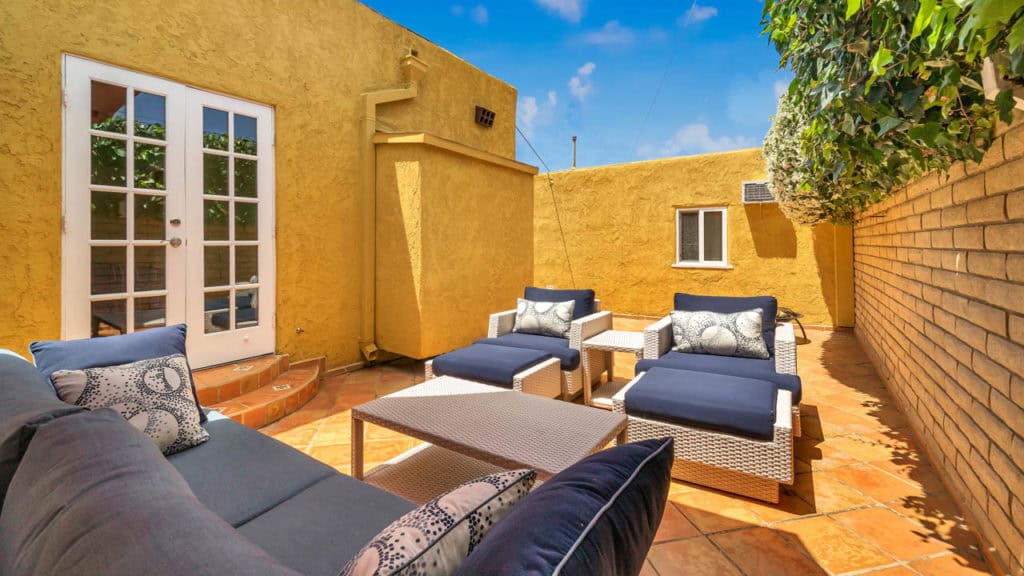 Private outdoor patio at 2212 Myrtle Ave in North Park featuring Saltillo tile, navy blue wicker lounge seating with ottomans, and a brick privacy wall under a bright blue sky.