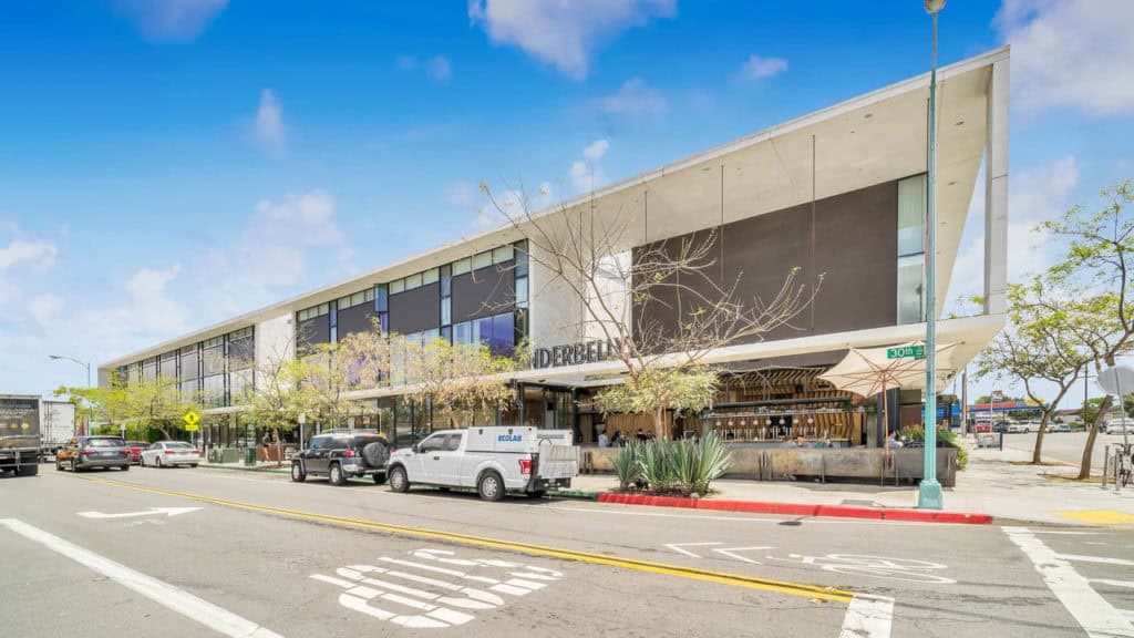 Exterior view of the Underbelly North Park restaurant at the corner of 30th Street and Upas Street, featuring a modern architectural design with an open-air bar and street-side patio.