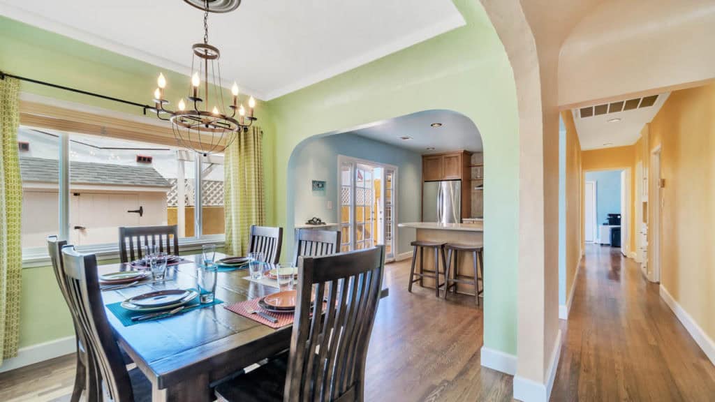 Formal dining room at 2212 Myrtle Ave in North Park with soft green walls, a dark wood dining set, and an arched view into a modern kitchen with stainless steel appliances.
