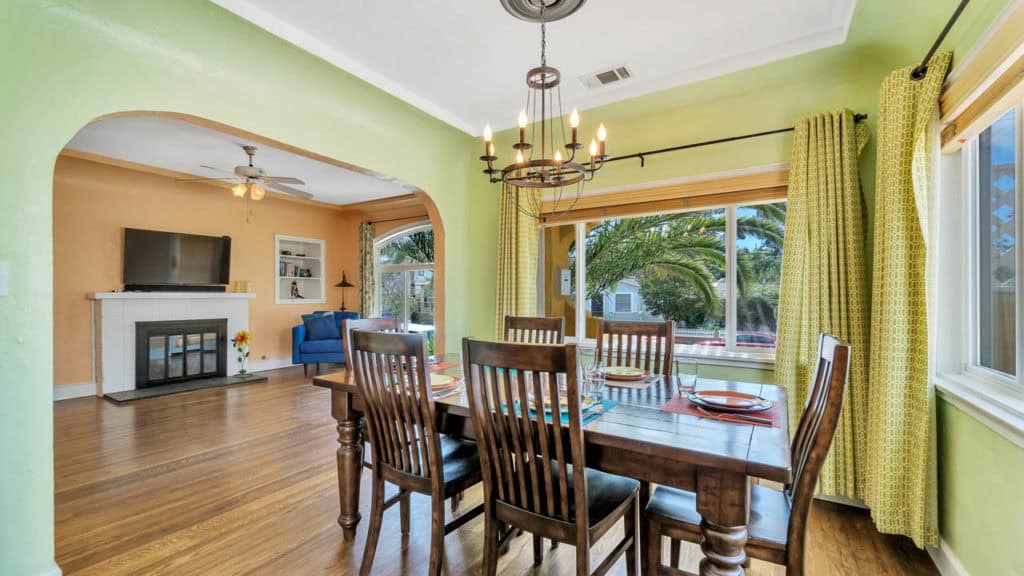 Formal dining room at 2212 Myrtle Ave in North Park featuring lime green walls, a wood dining table under a wrought iron chandelier, and an archway looking into the peach-toned living room.