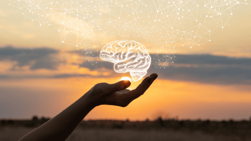 An open hand holding a graphic of a brain with a sunset as the background