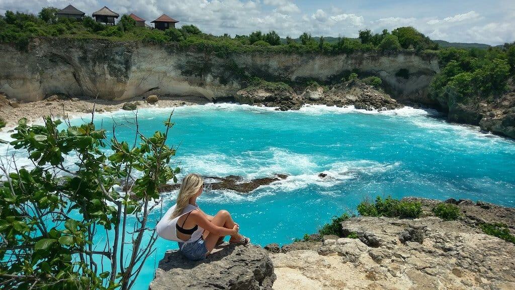 26 Beautiful Islands in Asia to Add to Your Bucket List 2024 8 girl sits on rock and looks out onto a bright blue lagoon and cliffs in Nusa Ceningan near bali in Indonesia, one of the most beautiful islands in asia