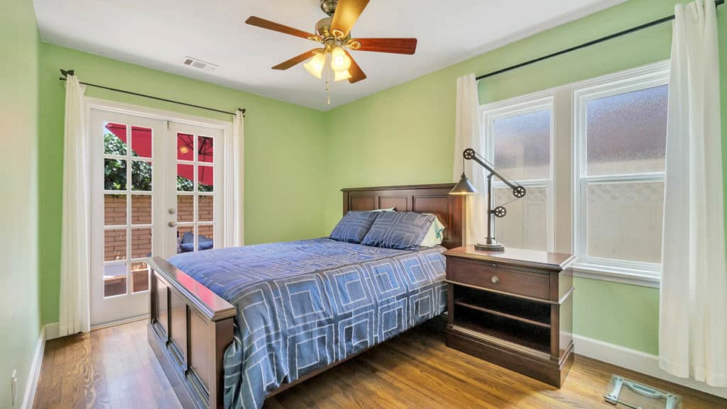 Bedroom at 2212 Myrtle Ave in North Park with sage green walls, a dark wood bed frame, and French doors leading out to a patio with a red umbrella.