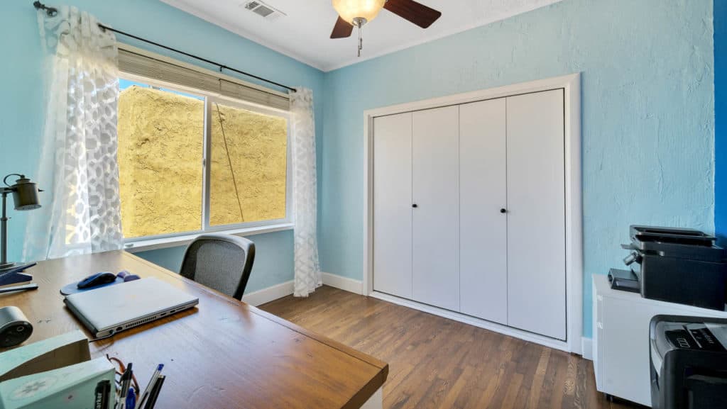 Home office at 2212 Myrtle Ave in North Park with light blue walls, a white bi-fold closet, hardwood floors, and a wood desk positioned near a window.