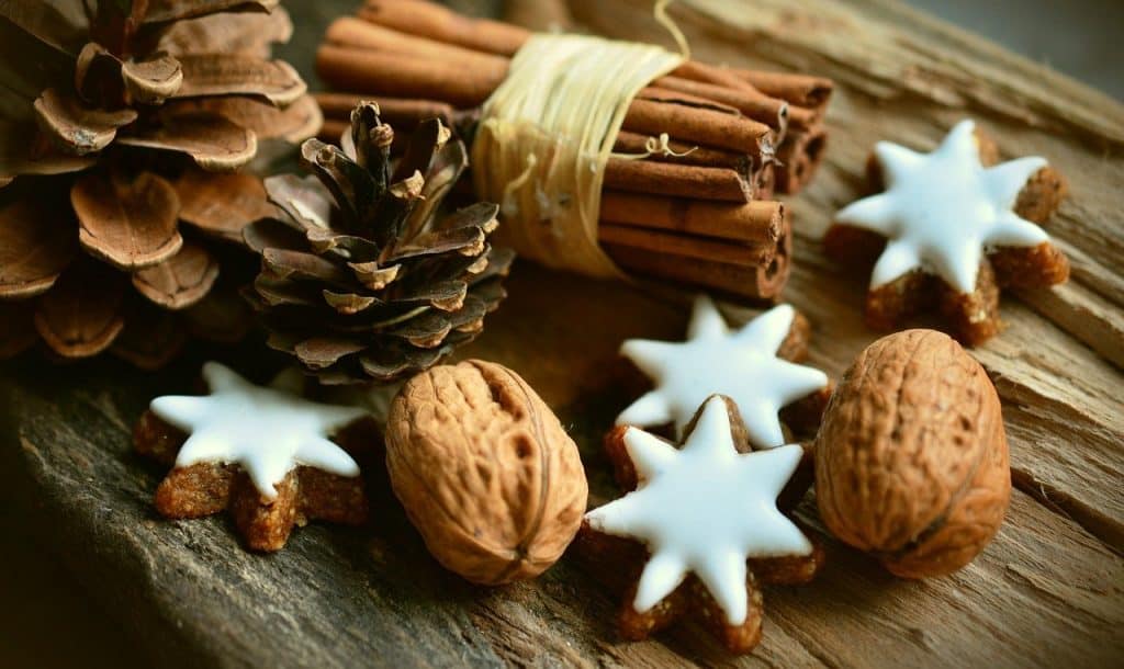 Sprigs of cinnamon, star-shaped cookies with white icing, walnuts, and pinecones arranged on rustic wooden surface for holiday or winter celebration.
