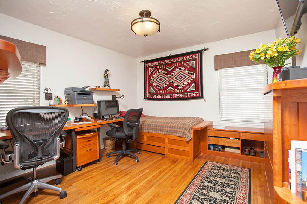 Home office and guest room at 3317-3319 Boundary Street in North Park featuring custom built-in wood cabinetry, a dual-desk workspace with ergonomic chairs, and a twin bed with a Southwestern-style wall hanging.