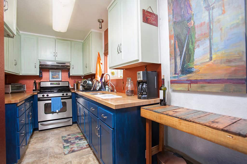 Galley kitchen at 3317-3319 Boundary Street in North Park featuring two-tone cabinetry with blue lowers and mint green uppers, butcher block countertops, and stainless steel appliances.