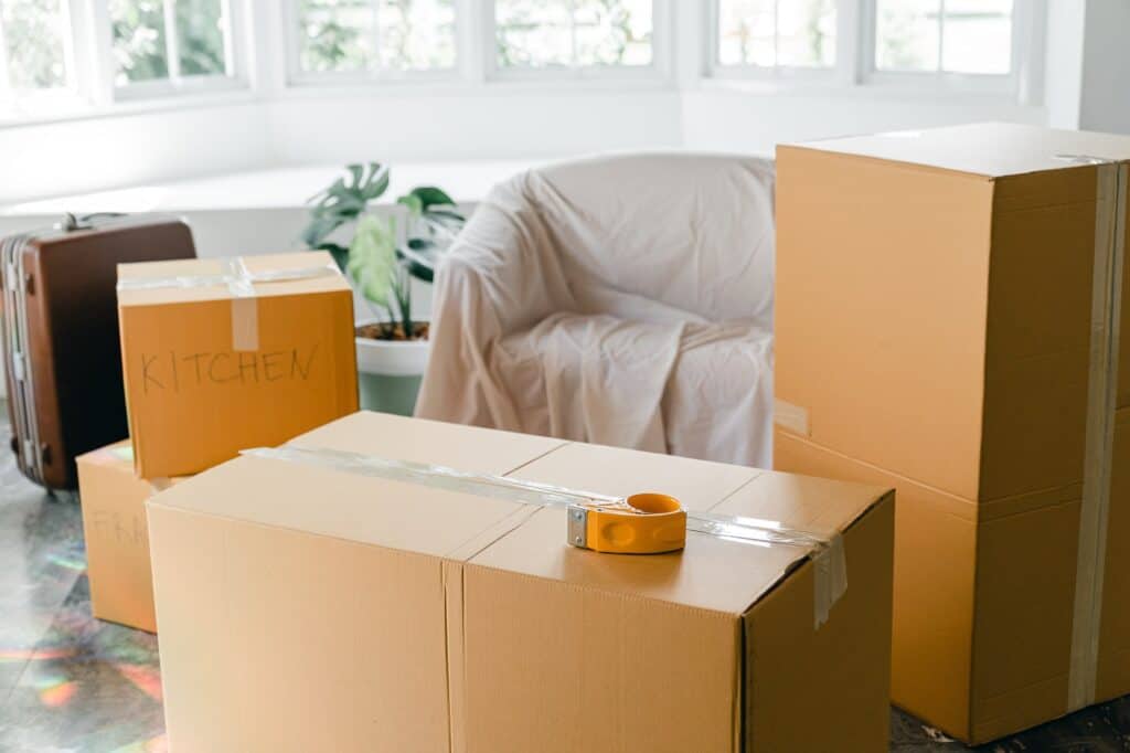 Cardboard moving boxes labeled "Kitchen" and a tape dispenser in a room.