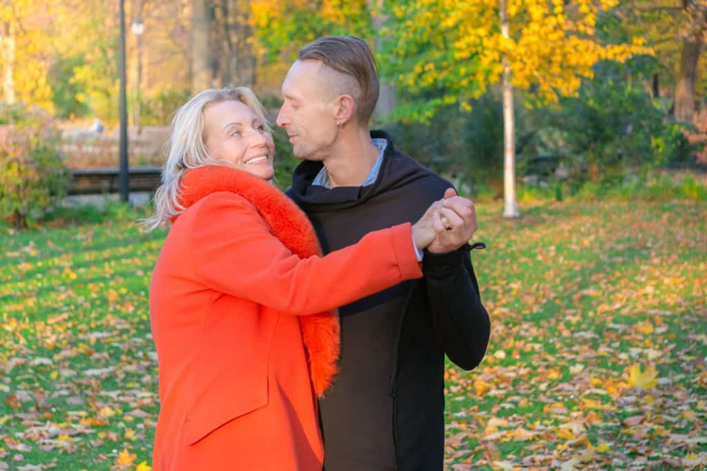 A mature couple dancing amongst fallen leaves basking in their long-lasting love.