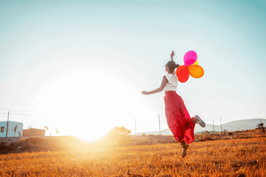 Woman holding colorful balloons running in a field at sunset, symbolizing joy and freedom.
