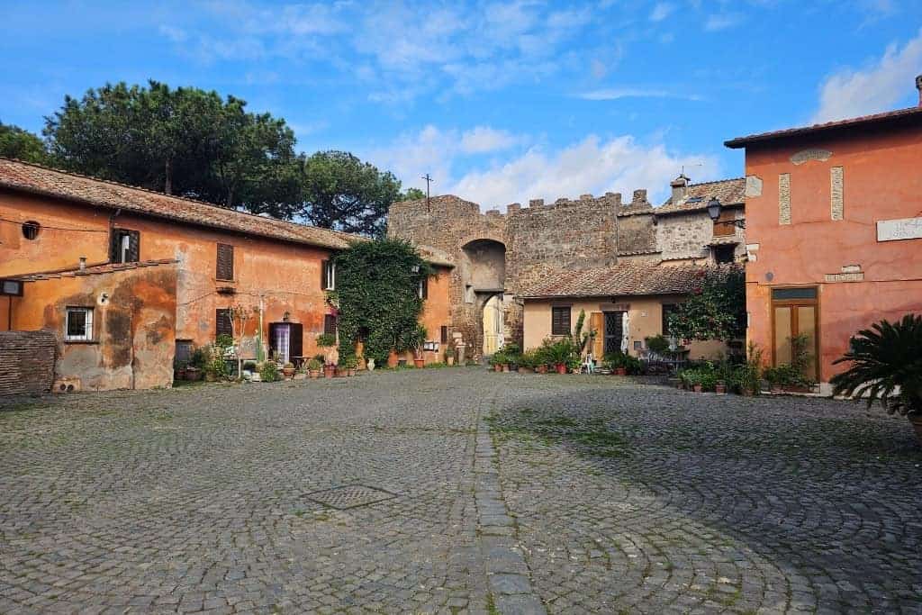 Picturesque cobblestone square in the old town of Borgo di Ostia Antica, near the ancient ruins, surrounded by rustic terracotta buildings.