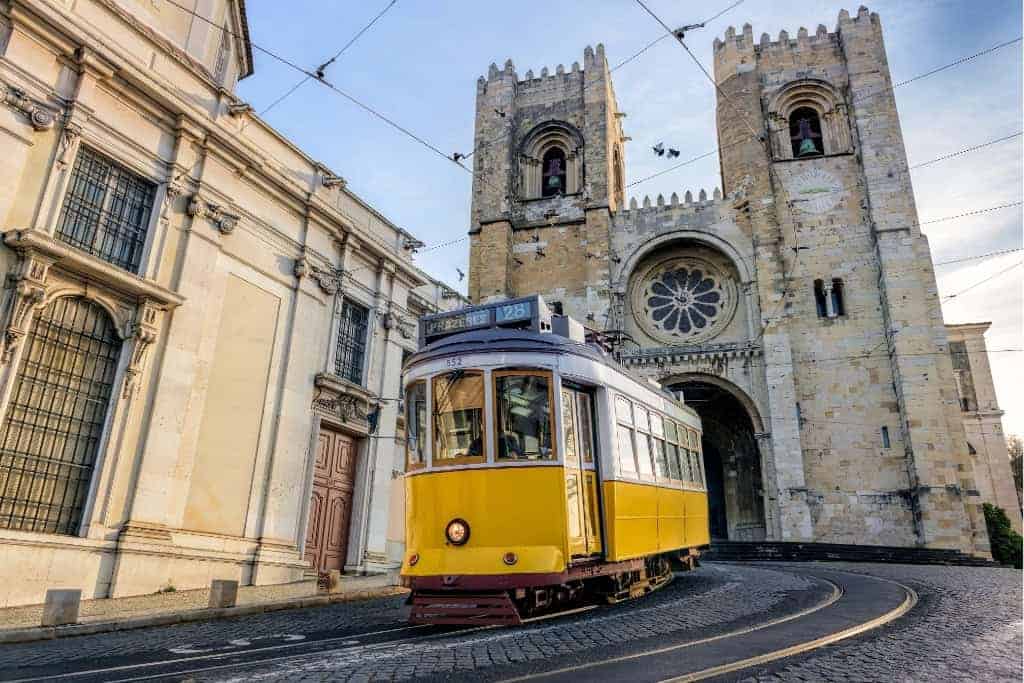 The iconic Tram 28 passing by the historic Sé de Lisboa (Lisbon Cathedral). Riding this tram is one of the best experiences to include in a Lisbon itinerary, offering a scenic journey through the city’s old neighborhoods.