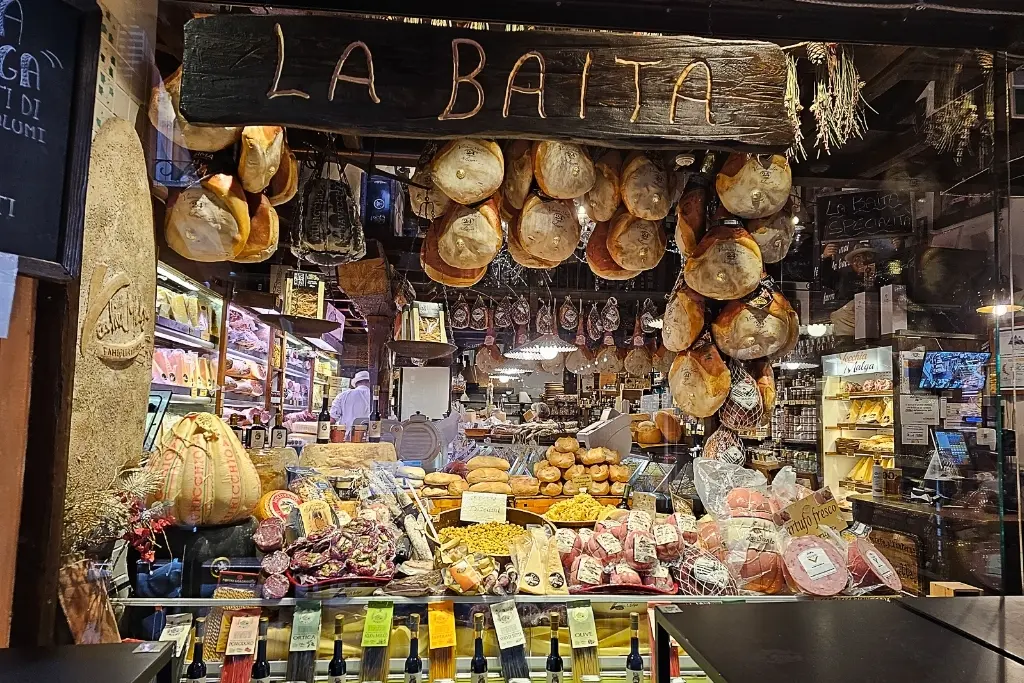 Window display of La Baita, a popular delicatessen in Bologna’s Quadrilatero Market, overflowing with Parmigiano Reggiano, prosciutto, mortadella, and regional food products—ideal for foodie photos.