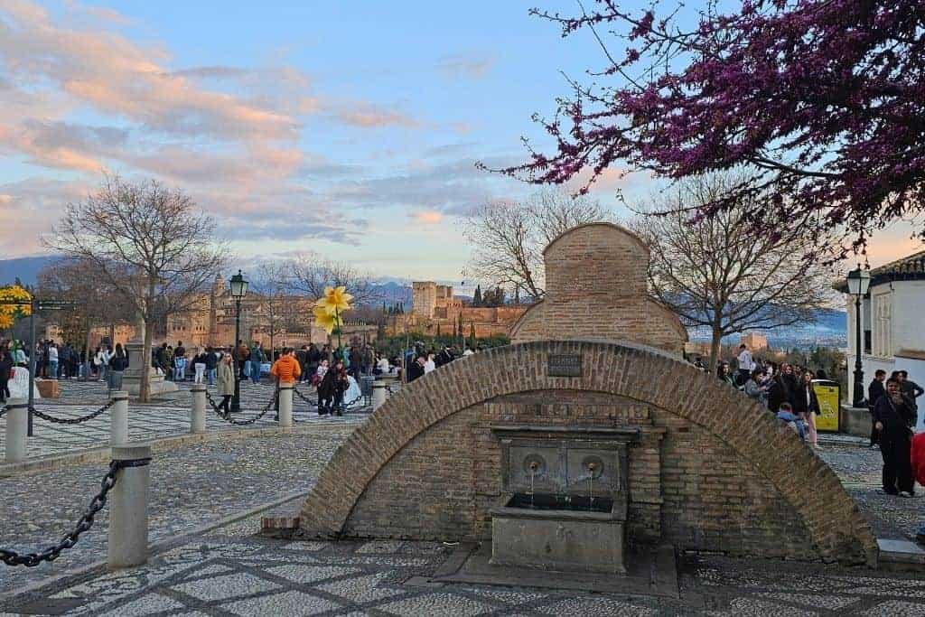 Aljibe de San Nicolás in Granada’s Albaicín neighborhood at sunset, with panoramic views of the Alhambra and the Sierra Nevada in the background – one of the best hidden gems in Granada for photography lovers.