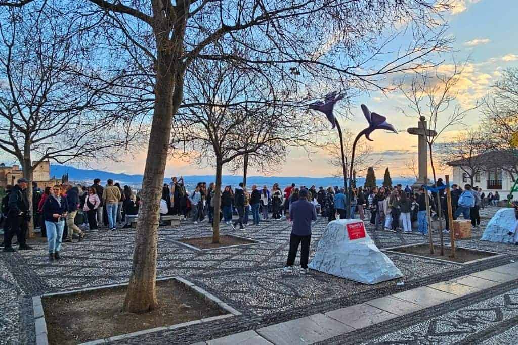 Sunset crowd gathering in front of San Nicolás Church at Mirador de San Nicolás, one of the best sunset spots in Granada with breathtaking views of the Alhambra and Sierra Nevada.