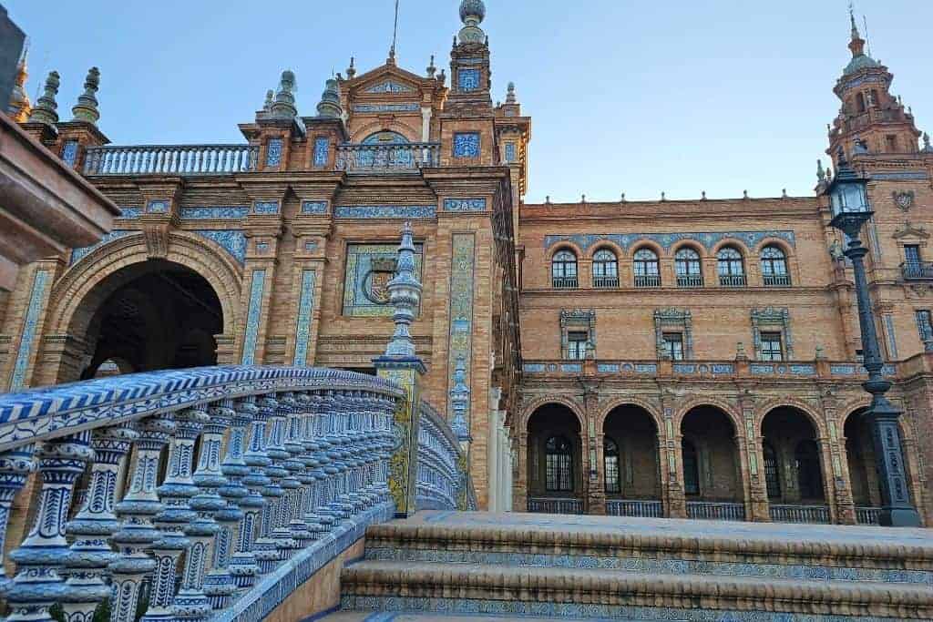 Close-up of the iconic blue-and-white ceramic bridge at Plaza de España in Seville, with ornate tilework and Renaissance Revival architecture glowing in the soft morning light — a must-see landmark often rushed through by first-time visitors.
