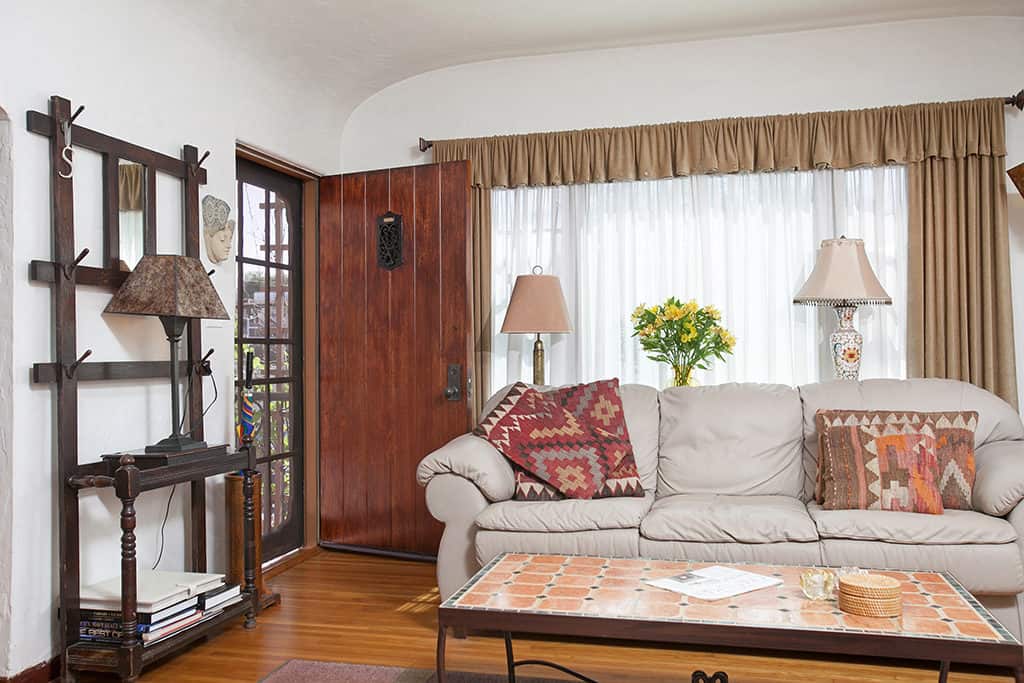 Living room entryway at 3317-3319 Boundary Street in North Park featuring original hardwood floors, a solid wood front door with a decorative speakeasy window, and a vintage-style hall tree next to a neutral sofa.