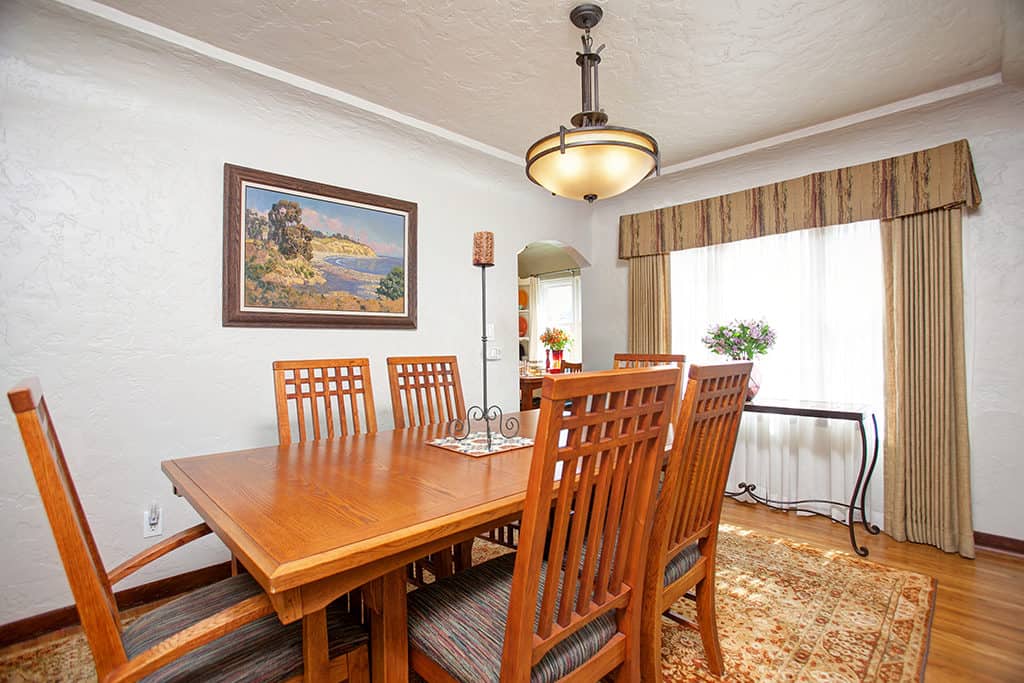 Formal dining room at 3317-3319 Boundary Street in North Park featuring a large wood dining table, Mission-style chairs, an elegant hanging light fixture, and an arched doorway leading to the living room.