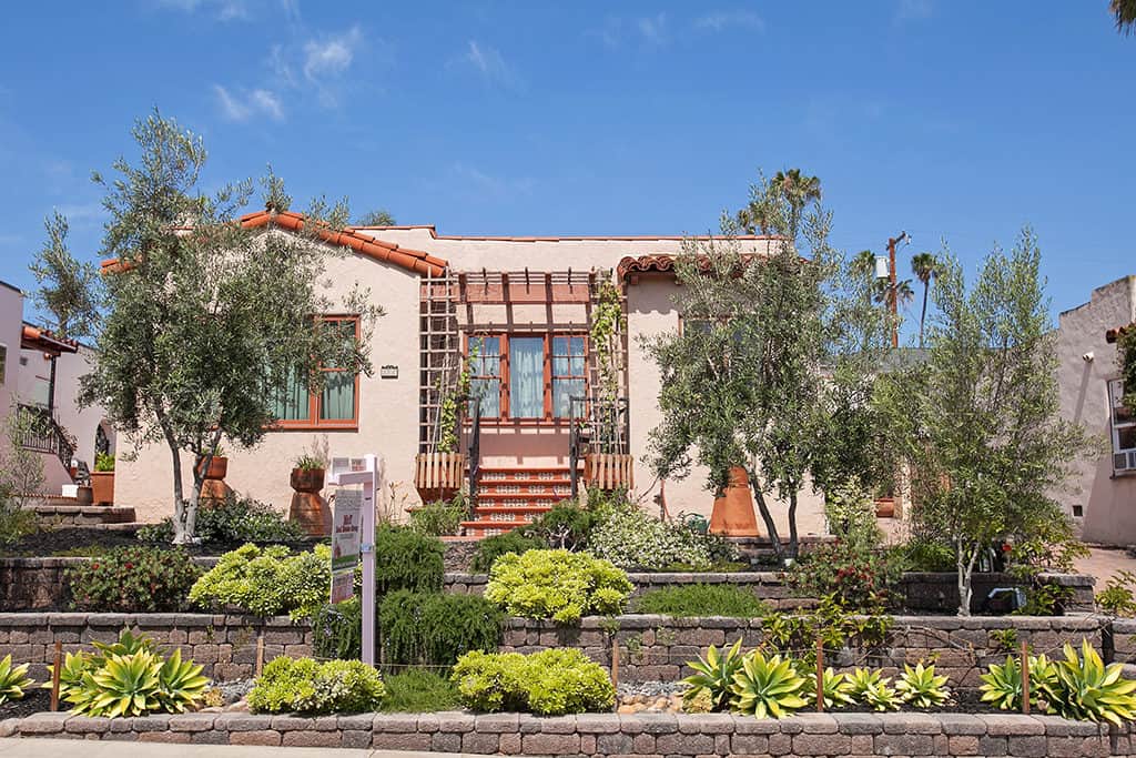 Spanish-style bungalow at 3317-3319 Boundary Street in North Park featuring a terracotta tile roof, decorative tile front steps, and drought-tolerant tiered landscaping with olive trees.