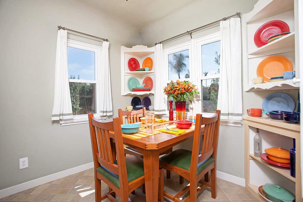 Sun-filled dining room at 3317-3319 Boundary Street in North Park featuring a wood dining table with green cushioned chairs and built-in corner shelving displaying a vibrant collection of colorful Fiestaware.