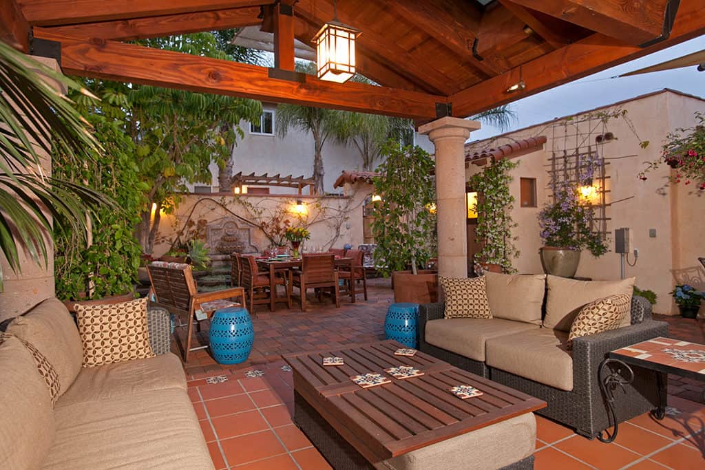 Covered outdoor living room at 3317-3319 Boundary Street in North Park featuring a vaulted wood-beam ceiling with hanging lanterns, terracotta tile floor, and comfortable wicker sofas overlooking the Mediterranean-style dining courtyard.