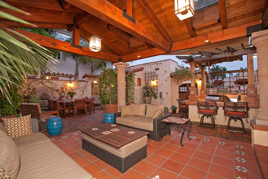 Spacious covered outdoor lounge at 3317-3319 Boundary Street in North Park featuring a vaulted wood-beam ceiling, terracotta tile flooring, wicker sofa seating, and a view of the adjacent outdoor kitchen and dining courtyard.