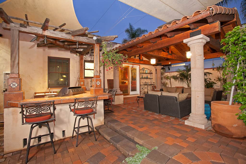 Outdoor kitchen and entertaining area at 3317-3319 Boundary Street in North Park featuring a built-in barbecue with bar seating, terracotta tile accents, a covered patio with a clay tile roof, and a shaded lounge area.