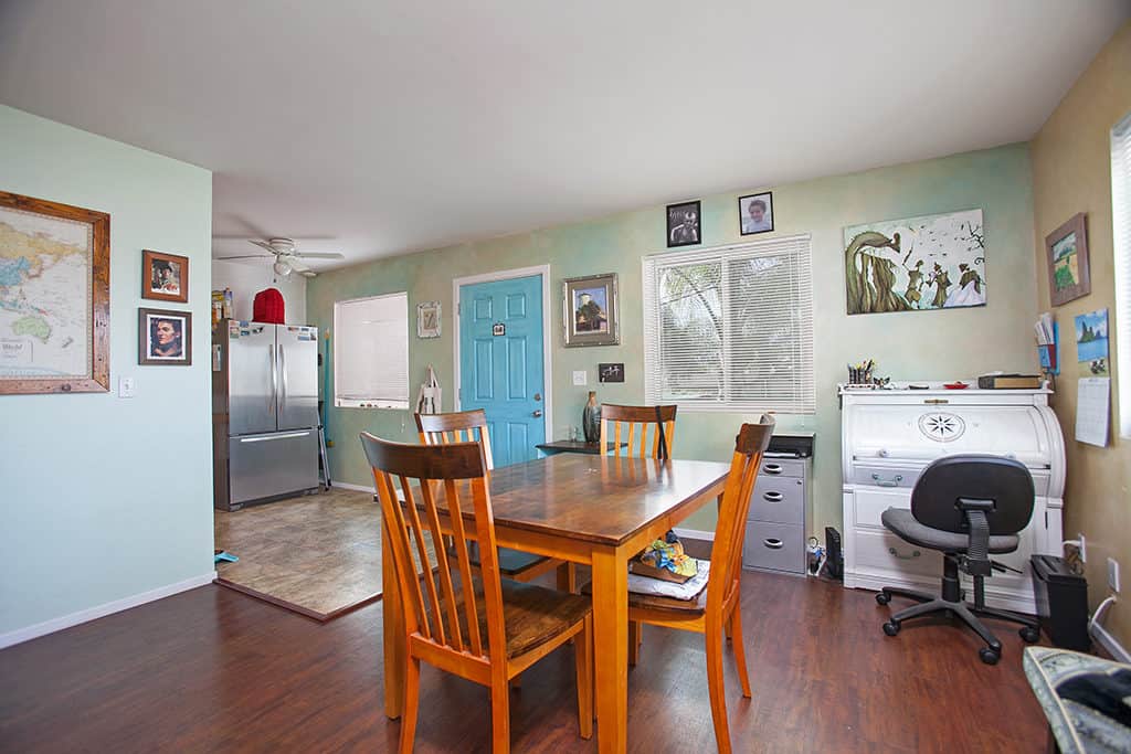 Open-concept dining and office area at 3317-3319 Boundary Street in North Park with a wood dining set, a white roll-top desk, and a bright blue entry door.
