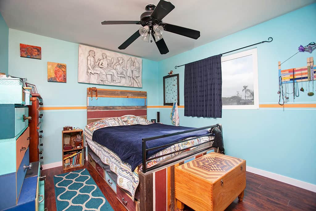Vibrant turquoise bedroom at 3317-3319 Boundary Street in North Park featuring a reclaimed wood headboard, colorful multi-tonal dresser, and a wood chest with an inlaid geometric design.