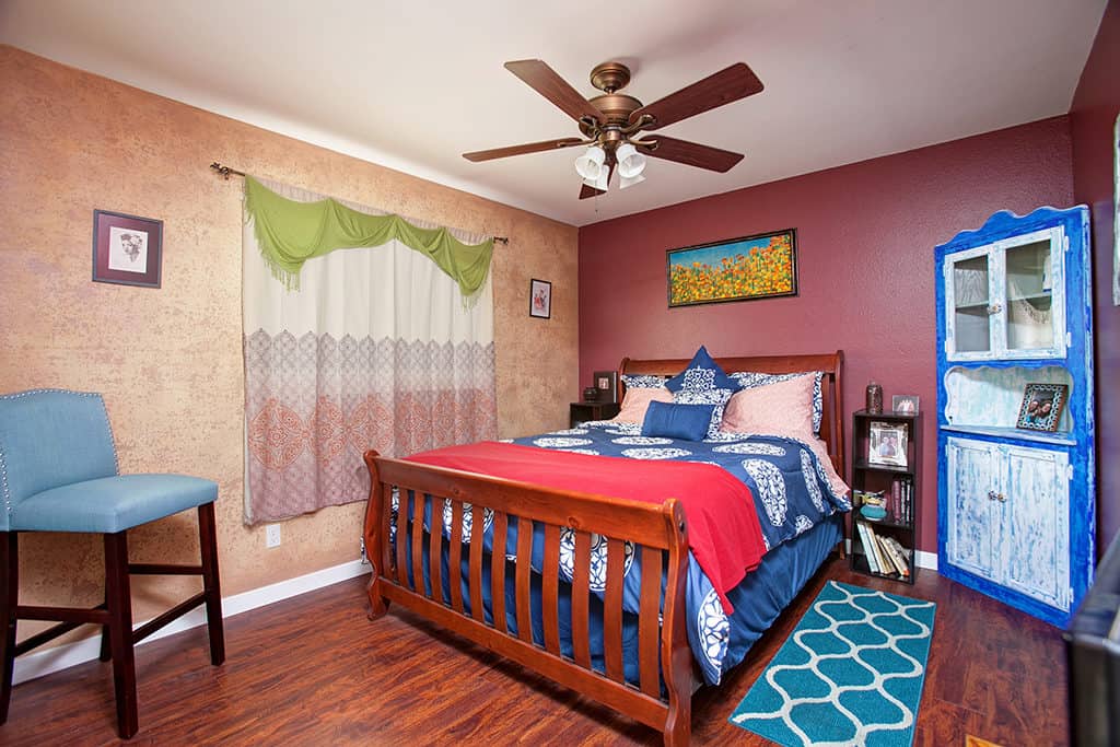 Eclectic bedroom at 3317-3319 Boundary Street in North Park featuring burgundy and textured beige walls, a wood sleigh bed with blue patterned bedding, and a vintage blue corner hutch.
