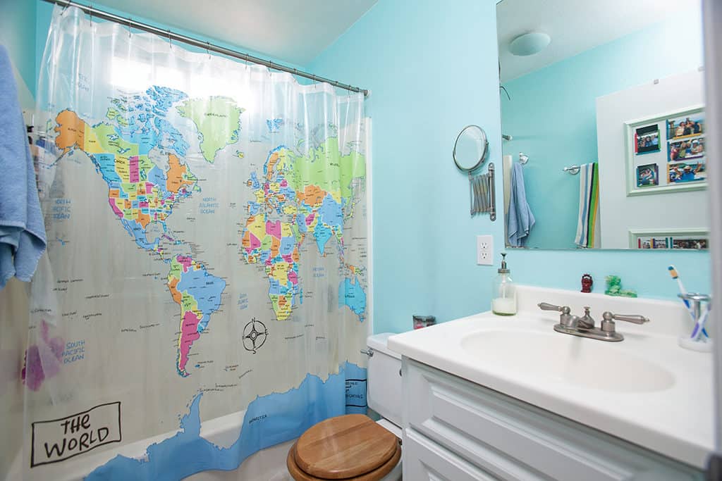 Bright blue bathroom at 3317-3319 Boundary Street in North Park with a white vanity, wood toilet seat, and a colorful world map shower curtain.