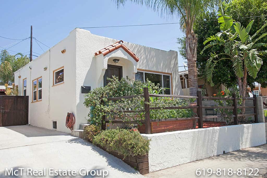 White Spanish-style bungalow at 3714 Dwight St in Cherokee Point with a red tile roof entry, wooden garden fence, and palm tree.