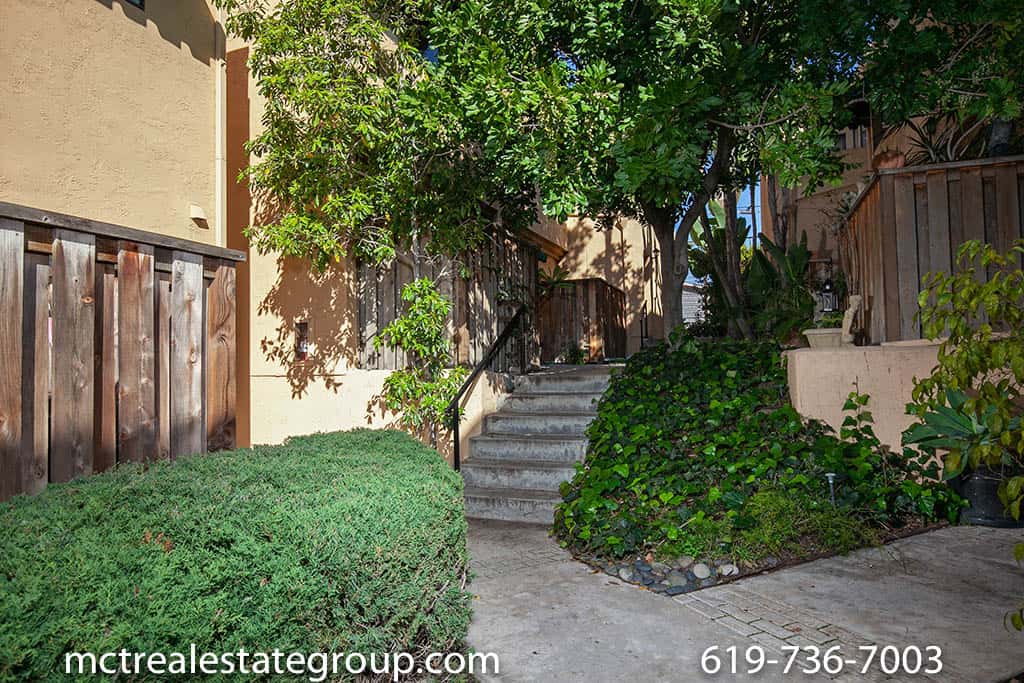 Lushly landscaped walkway at 3761 Villa Terrace in North Park featuring a concrete staircase, mature trees, and verdant hedges leading through a quiet, Mediterranean-style residential complex.