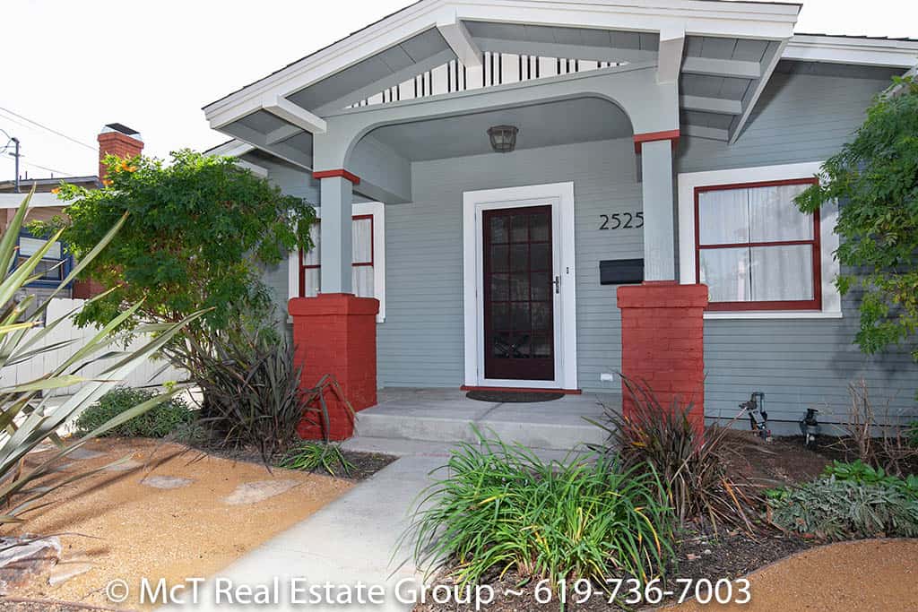 The exterior of 2525 Myrtle Avenue in North Park features a classic Craftsman-style porch with muted sage-toned siding, red brick pillars, and a glass-paned front door.