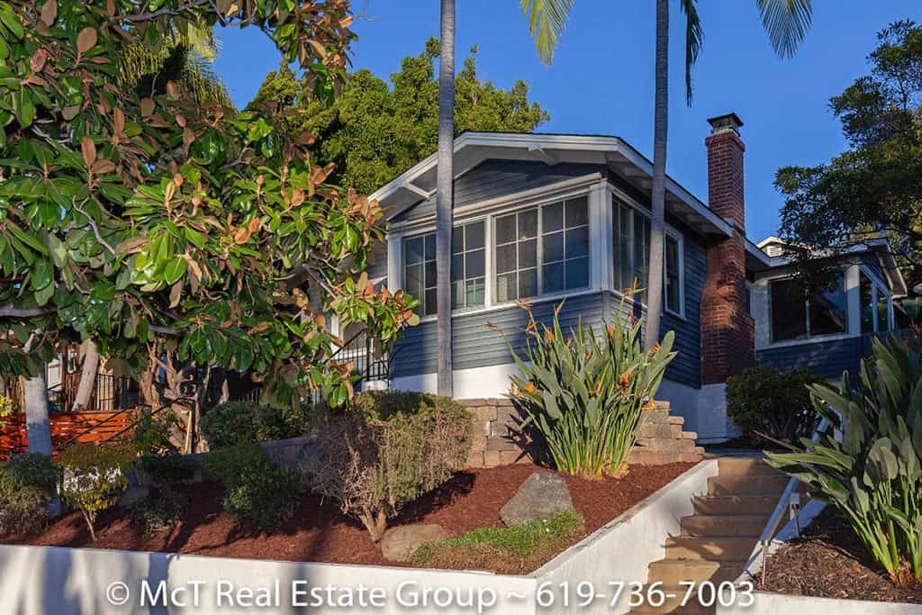 Exterior view of a blue Craftsman home with a sunroom, brick chimney, and tiered landscaping at 3629 Villa Terrace in North Park.