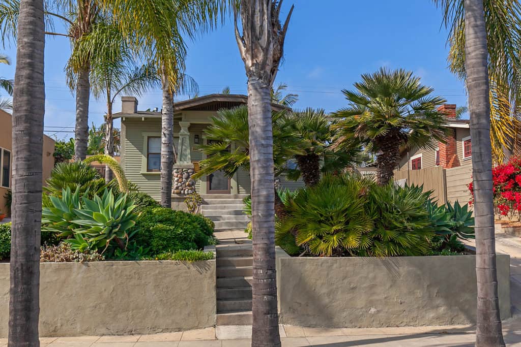 The front exterior is framed by tall palm trees and features a tiered garden with agave and lush greenery leading to a Craftsman-style porch at 3530 Arizona Street in North Park.