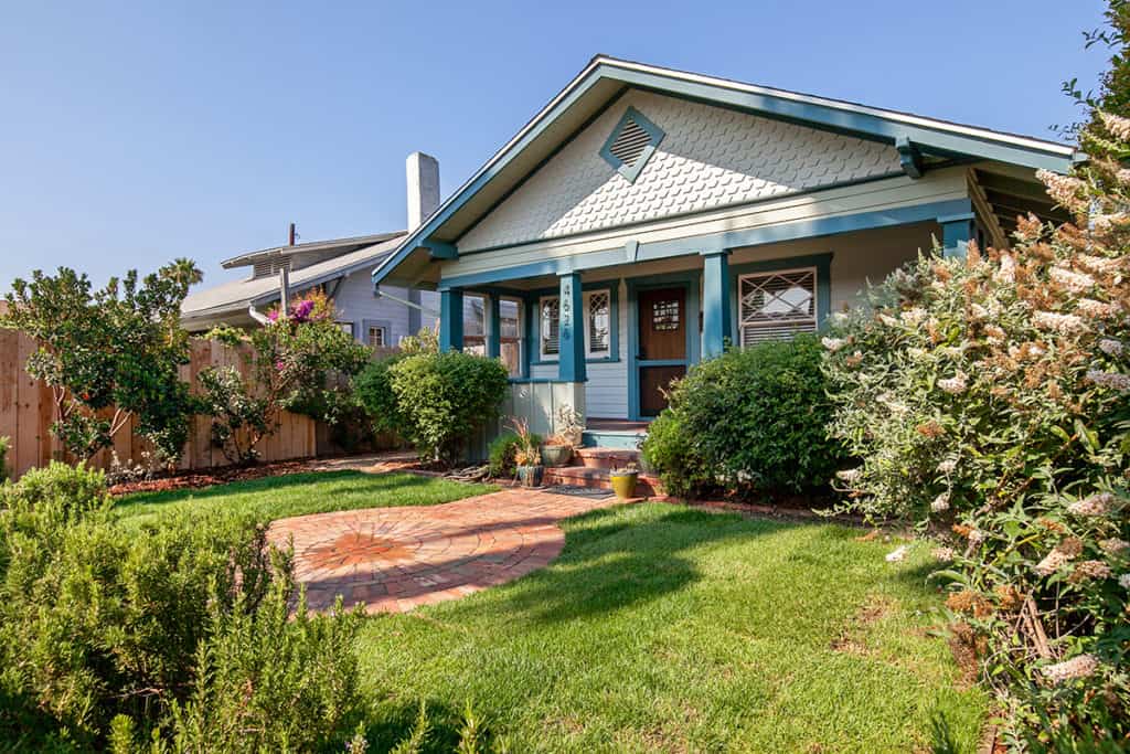 Charming Craftsman bungalow exterior featuring light blue siding, a circular brick paver patio, a green lawn, and a covered porch at 4626 Alabama Street in University Heights.