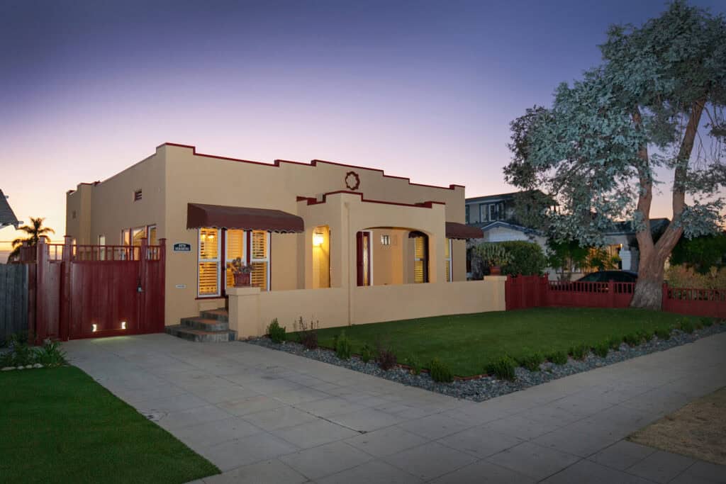 Single-story beige stucco house with a wooden side gate, green grass lawn, concrete driveway, and front porch at twilight at 3570 Pershing Avenue in North Park.
