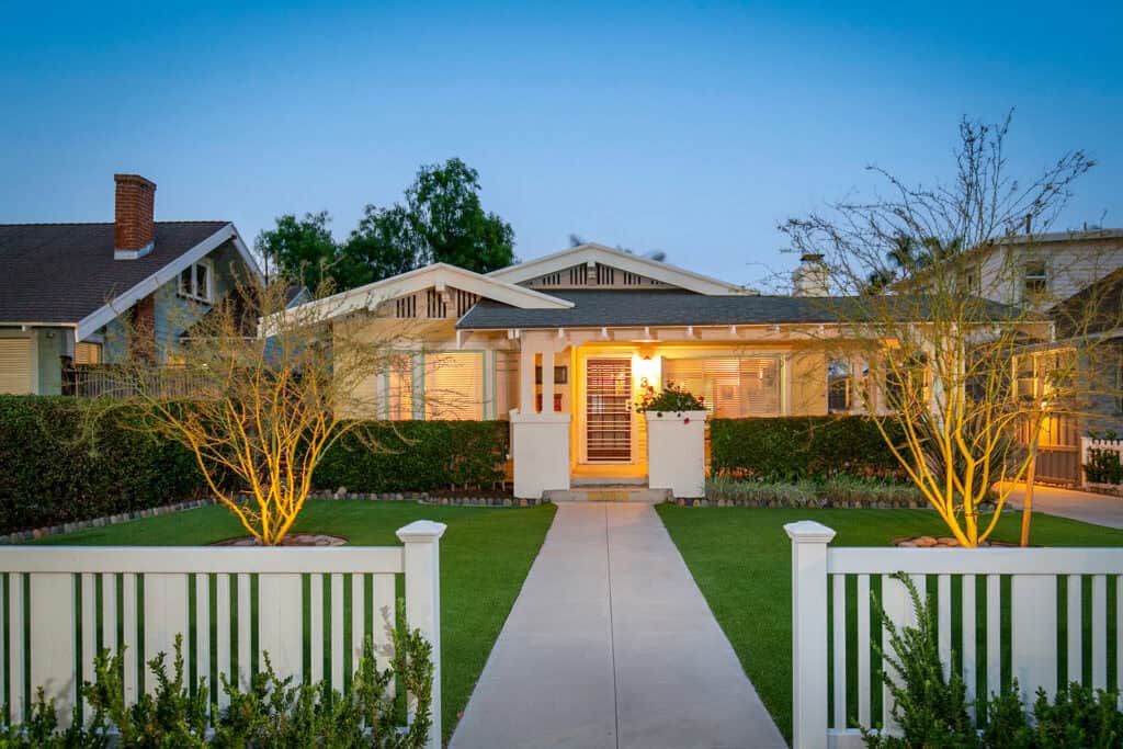 Craftsman home at dusk in North Park, San Diego with professional landscape lighting and a white picket fence