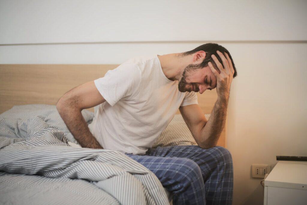 A Man Sitting on the Side of the Bed Holding his Head